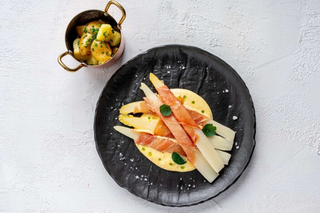 Vařený bílý chřest s holandskou omáčkou. Bílý chřest v parmské šunce je klasika a my ho v restauraci Na Krétě v menu 2026 podáváme s novými brambory. 